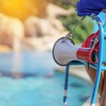 Lifeguard sitting on chair with megaphone at poolside