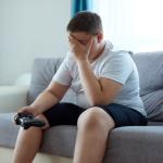Overweight boy sitting on a coach holding a video game controller
