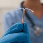 Doctor holding T-shaped intrauterine birth control device on blurred background, closeup