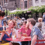 Waitress offering Zilveren Kruis sunscreen to people on a terrace