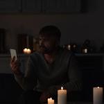 Power outage - Man looking at mobile phone while sitting in dark kitchen near burning candles