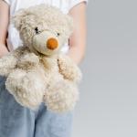 Partial view of child holding teddy bear isolated on grey