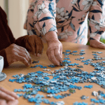 Selective view of four elderly people sitting at a table and building a puzzle
