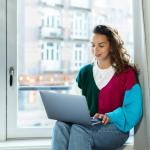 A woman working on a laptop while sitting on a windowsill