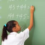 Primary school girl writing maths answer on chalkboard
