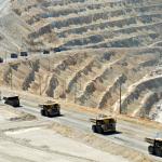 A long line of monster dump trucks carrying loads of rock out of an open pit copper mine
