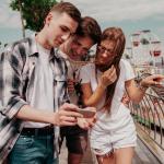 A young man shows something to his friends on his phone.