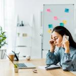 A woman appears stressed as she sits in front of her laptop while speaking on the phone.