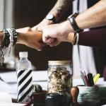 Five men and women fist bump after making a business deal