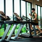 A man running on a curved treadmill inside a fitness center, with a massage table and weight bench
