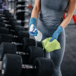 Partial view of a woman cleaning equipment in a gym with sanitizer