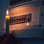 A candle is used to inspect a fuse box during a power outage.