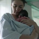 A mother and newborn baby, wrapped in a striped hospital gown