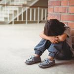 A sad child sits alone in a school corridor.