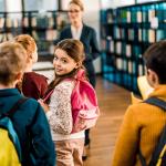 Boys and girls enter a classroom and are greeted by their teacher.