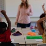 Back view of children in a primary school classroom raising their hands to answer the teacher's question