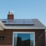 Solar Panels on the roof of brick home with Adirondack garden chairs in front of a window. 2019