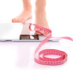 Female feet stepping onto a bathroom scale with measuring tape nearby