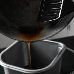 Pouring used cooking oil from frying pan into container