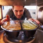 A man is taking a plastic container out of the microwave