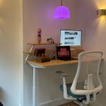 The Flexispot E7Pro desk and Flexispot SHEER office chair, with a Mathmos Lava Lamp, Macbook Air, Asus monitor, KLM collectible canal houses, and a small decanter in a stack of fake books. January 2026
