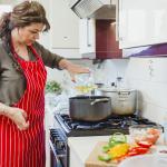 Woman cooking in the kitchen, adding oil to the pot with sliced up bell peppers on the counter