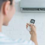 An image showcasing a woman using a remote control to adjust a wall-mounted air conditioner.