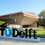 A TU/Delft sign on the university's campus in front of the auditorium.