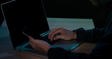 A man using his laptop and mobile phone to perform cybercrime activities.
