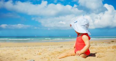 A young baby sits on a sunny beach in southern France in 2021