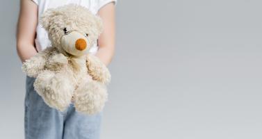 Partial view of child holding teddy bear isolated on grey