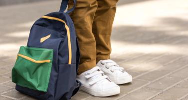 Cropped picture of a child standing next to a backpack