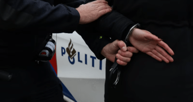 Arrest: Police officer handcuffing a suspect with a police car in the background