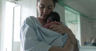 A mother and newborn baby, wrapped in a striped hospital gown