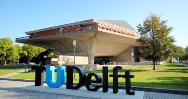 A TU/Delft sign on the university's campus in front of the auditorium.
